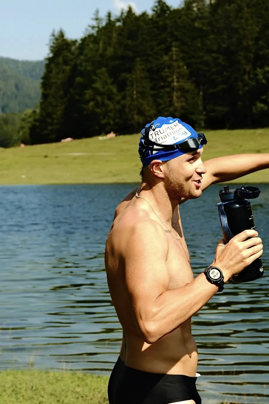 Hans-Jörg Stolz kommt mit Badekappe aus einem Bergsee, dahinter Almwiese und Wald