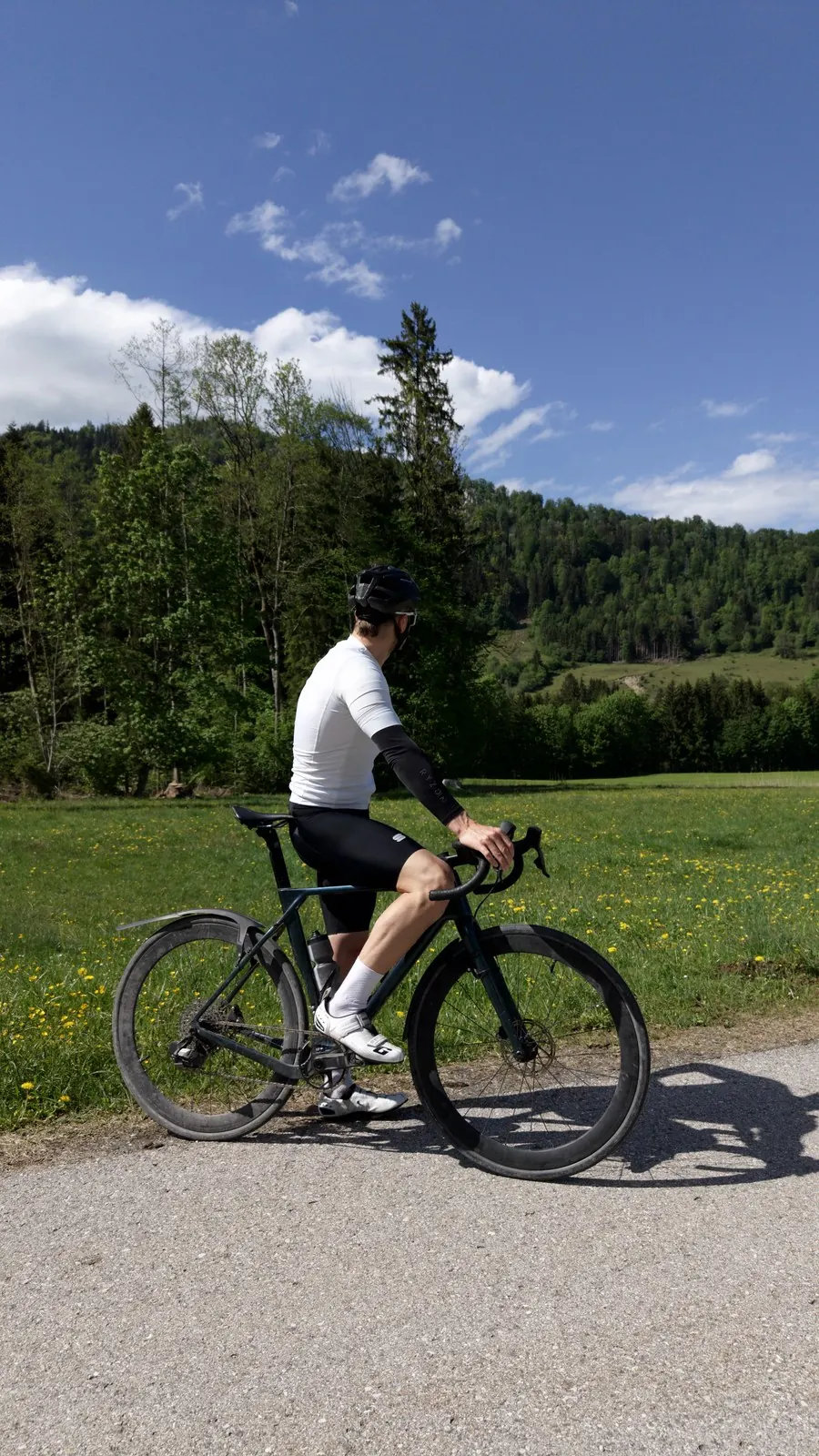 Hans-Jörg Stolz auf dem Rennrad an einer Wiese, dahinter Wald und Berge