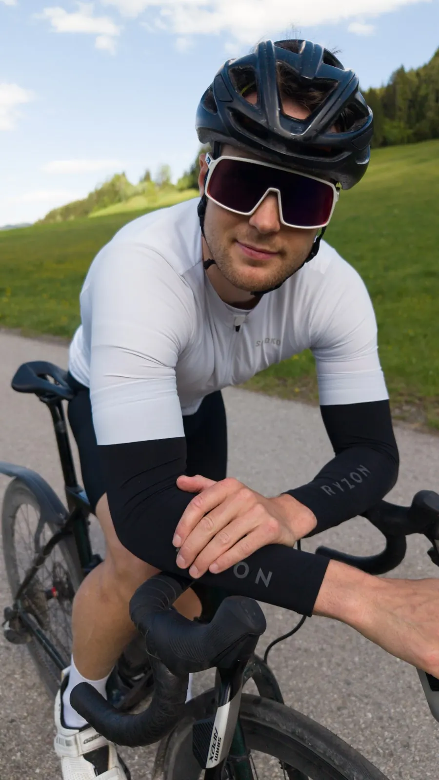 Hans-Jörg Stolz auf dem Rennrad, Helm und Sportbrille, im Hintergrund eine Wiese