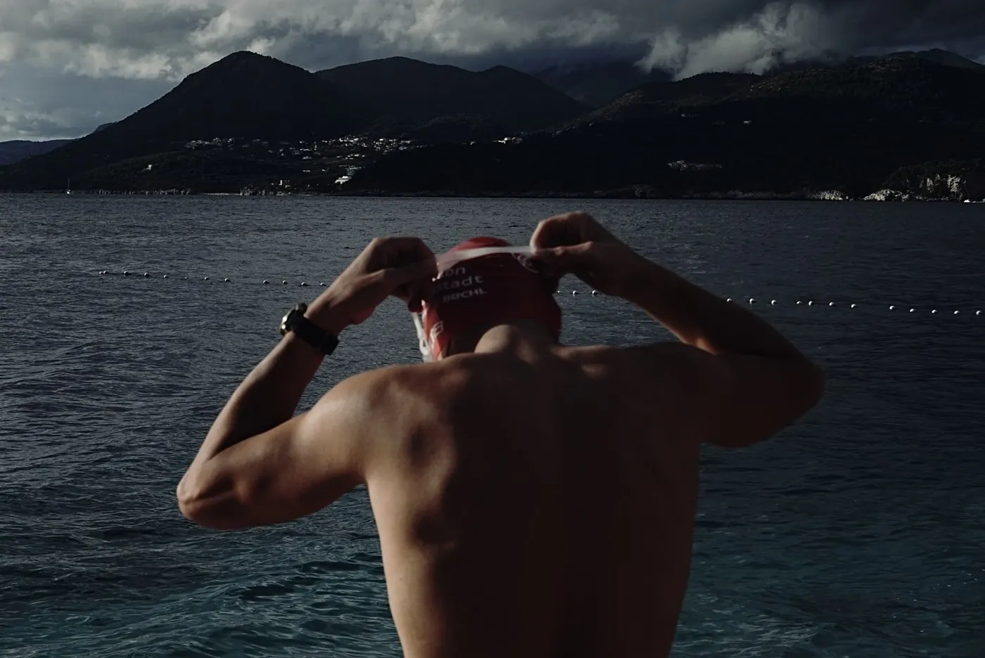 Hans-Jörg Stolz zieht sich vor dem Schwimmstart die Badekappe zurecht, dahinter aufziehendes Wetter über der Küste